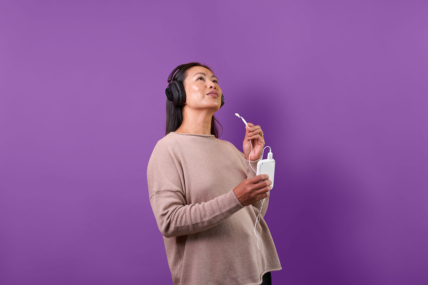 A standing woman is holding Lunire tinnitus device and glancing upward with a slight smile.