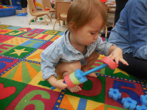 Small child sliding pool noodle slices onto a stick to practice fine motor skills and problem solving