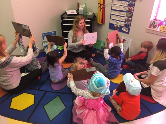 Teacher and kids seated in a circle on the floor using dry erase boards