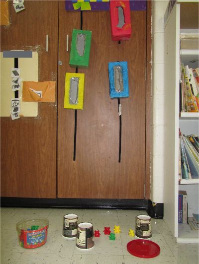 Colored tissue boxes velcroed vertically on a cabinet with container a container of small shapes on the floor