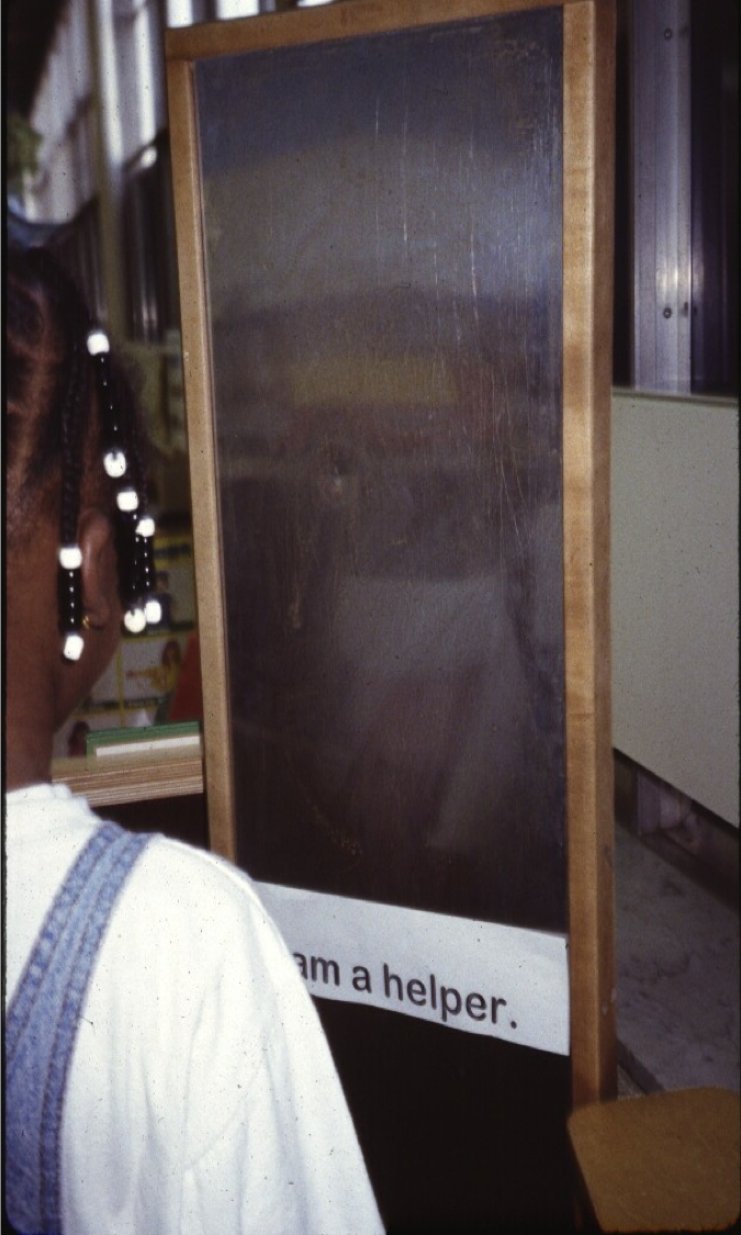 Child affirmation exercise in front of mirror with an I am a helper sticker on the mirror