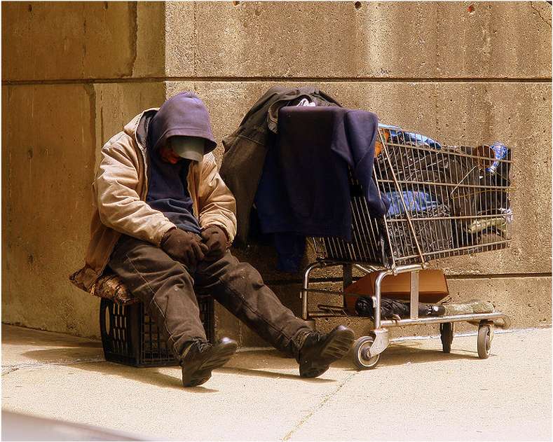 Man sitting on a crate with a grocery cart full of personal items