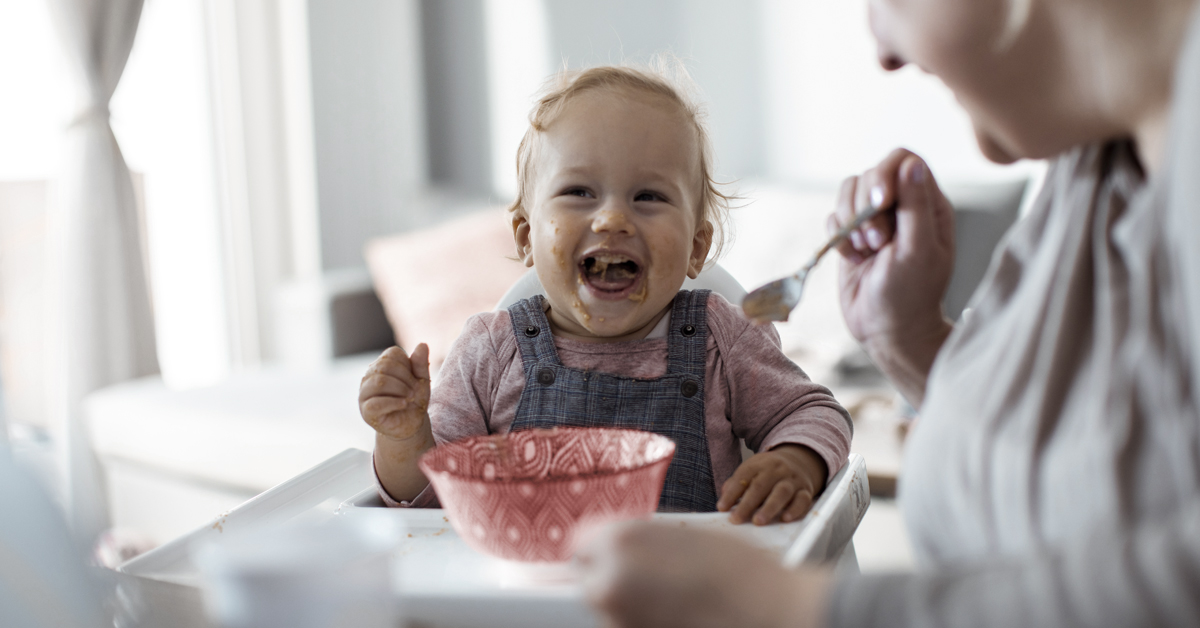 An adult feeding a child in a highchair 