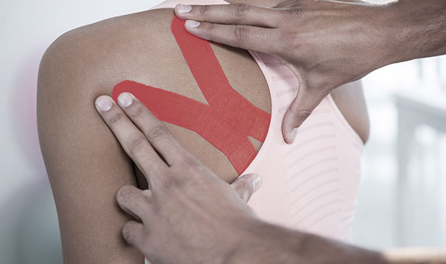 occupational therapist applying x-shaped kinesiology sports tape to a client&rsquo;s left shoulder