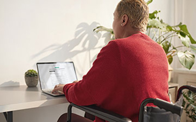 woman in wheelchair is at her desk signing up for a continued membership on laptop