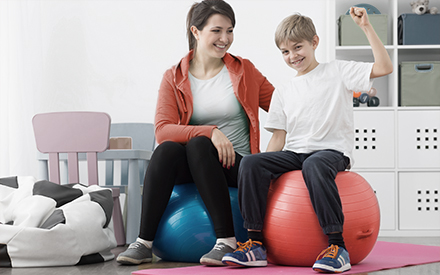 an occupational therapist and child sit side-by-side on separate ball chairs