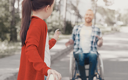 a child plays catch with a person seated in a wheelchair